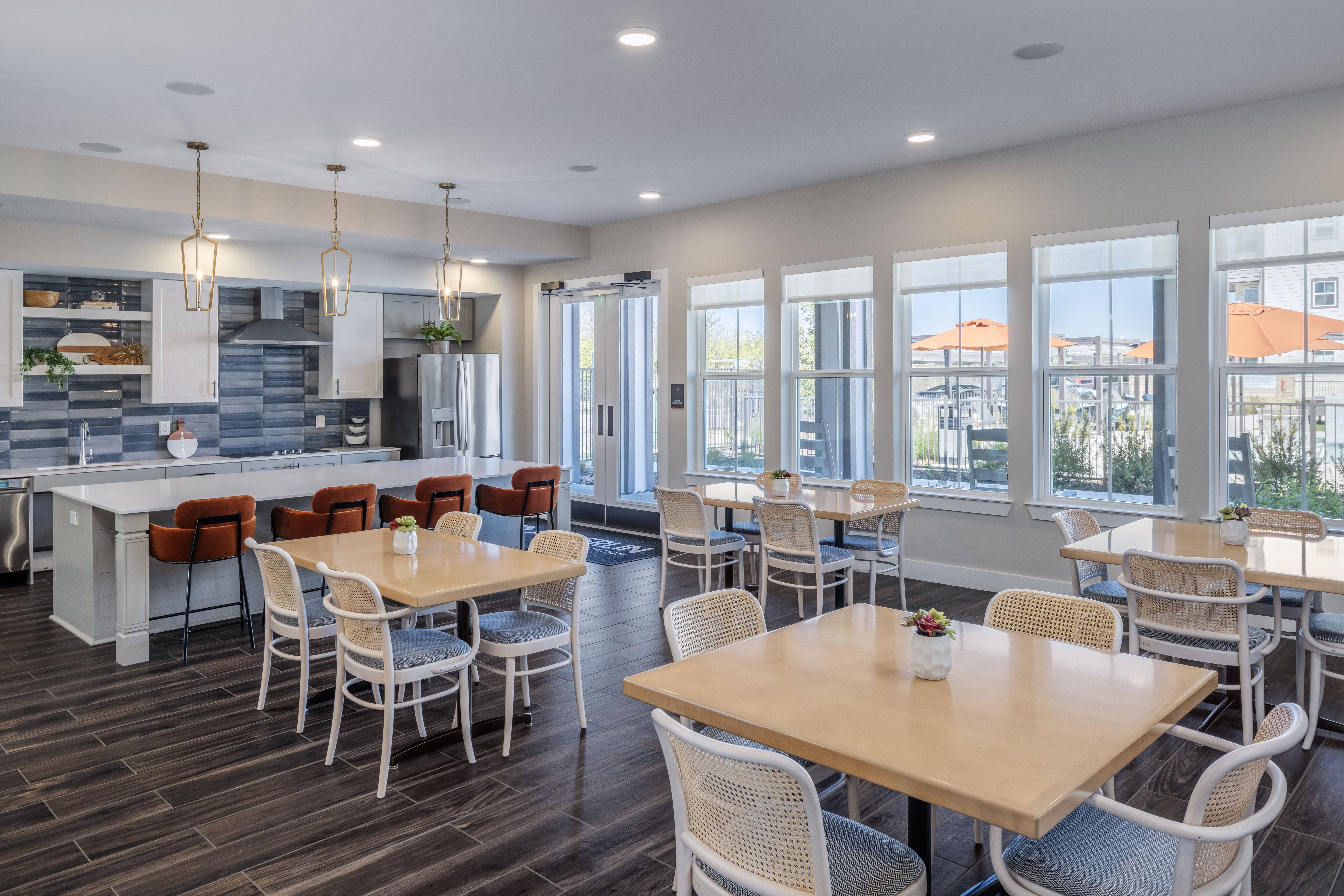an open dining room and kitchen area with dining tables and chairs at a senior apartment community